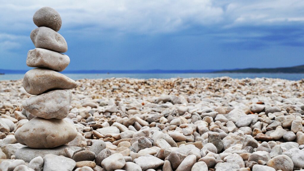 Balanced smooth stones on a pebbled beach under a dramatic cloudy blue sky wallpaper background