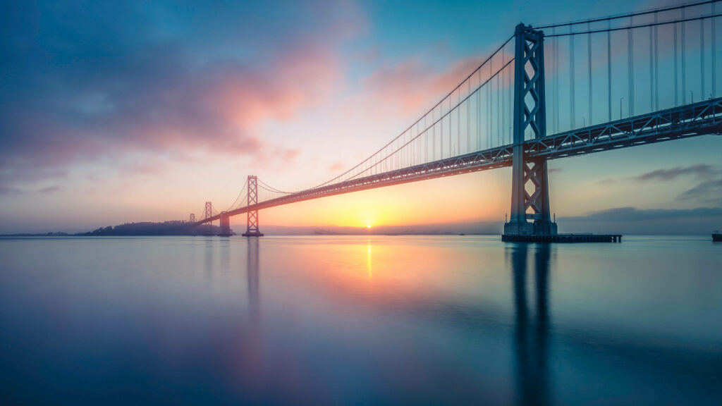 Tranquil Bay Bridge Sunset Wallpaper: Soft Hues Over Calm Waters