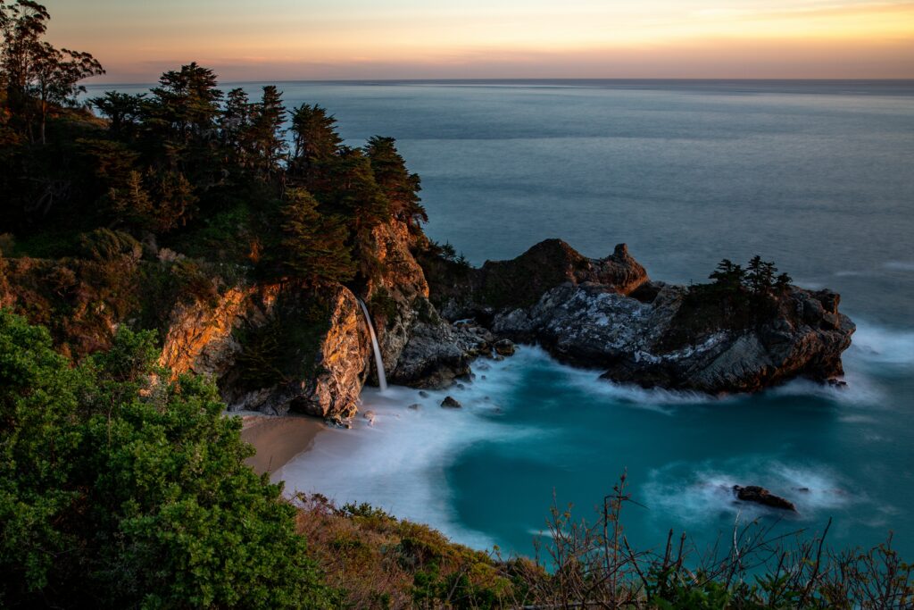 Sunset bay wallpaper with waterfall rocky cliffs turquoise sea sandy shore lush trees