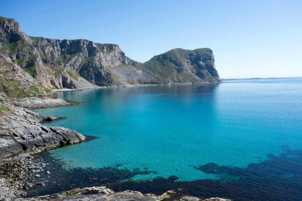 Tranquil bay with turquoise waters and rugged mountains under bright blue sky wallpaper background