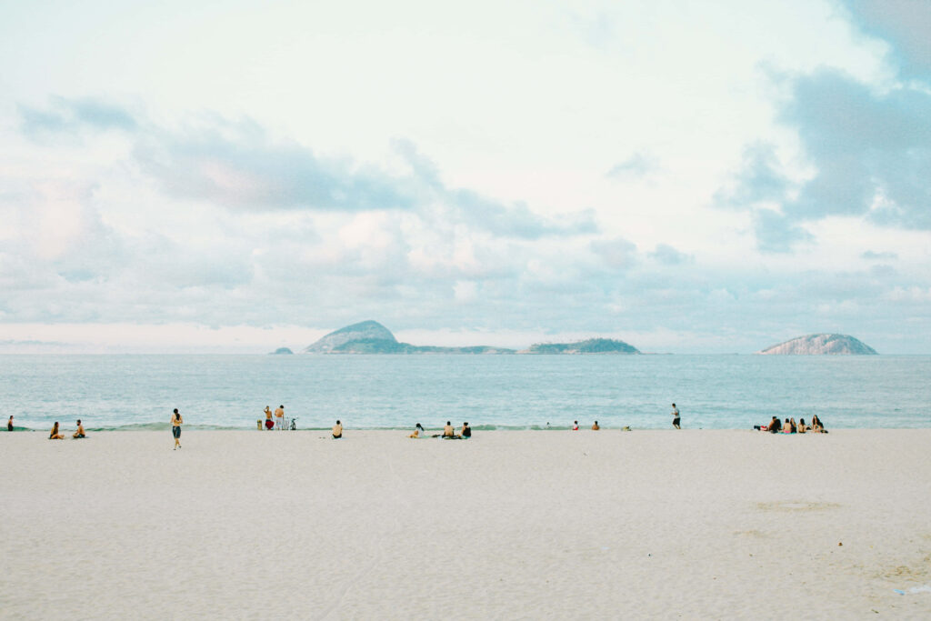 Tranquil Beach Scene: People Enjoy Peaceful Day with Distant Islands Wallpaper