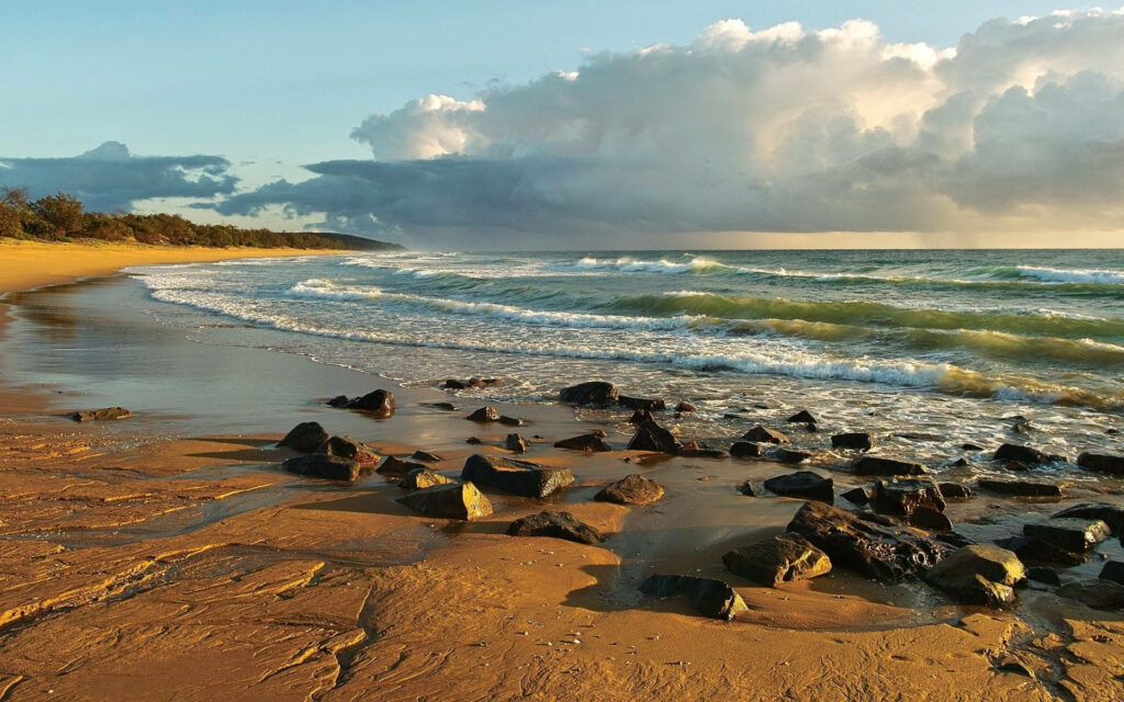Tranquil Beach Scene Wallpaper: Rocky Shoreline & Dramatic Clouds