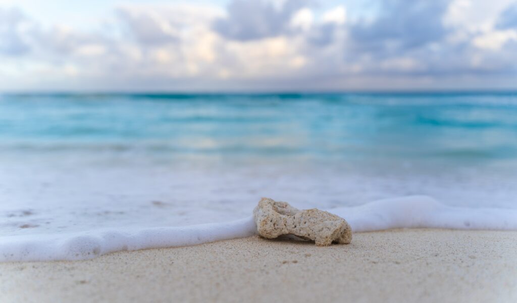 Tranquil beach with single stone soft sand gentle waves foamy edges calm turquoise sea horizon Wallpaper