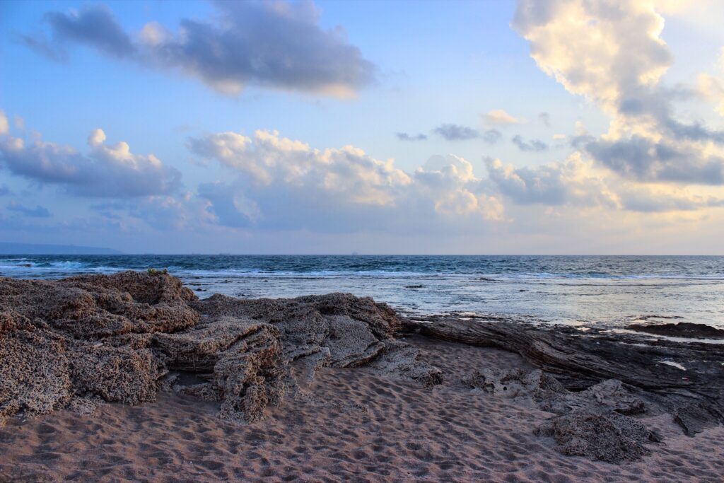 Tranquil beach with soft sand rugged rocks gentle waves and warm glowing sky at sunrise or sunset Wallpaper