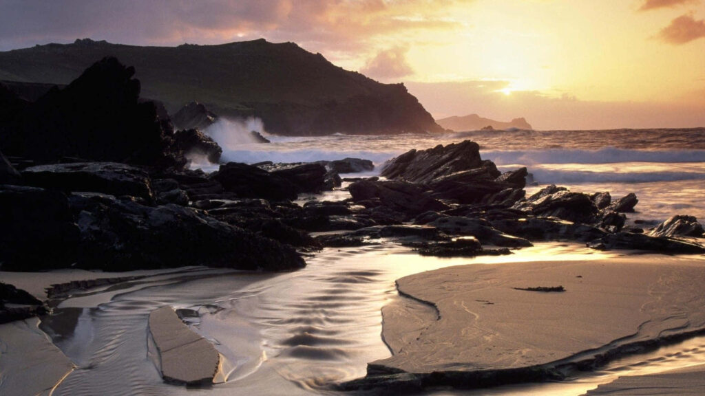 Tranquil Deserted Beach Sunset: Rugged Rocks & Gentle Waves Background Wallpaper
