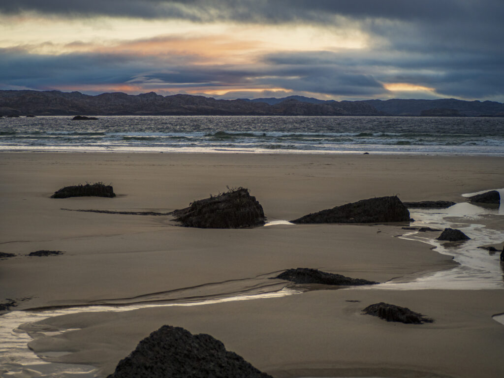 Tranquil beach sunset wallpaper with smooth sand rocks gentle waves and soft orange blue hues