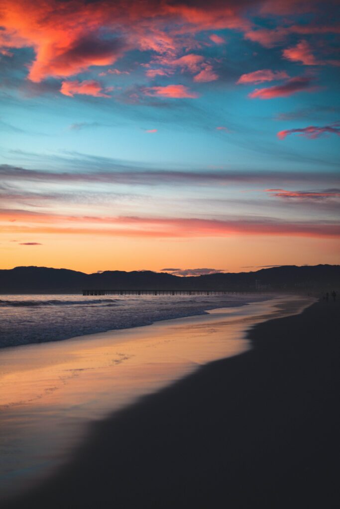 Sunset beach wallpaper with orange pink clouds mountains silhouette and gentle waves on shore