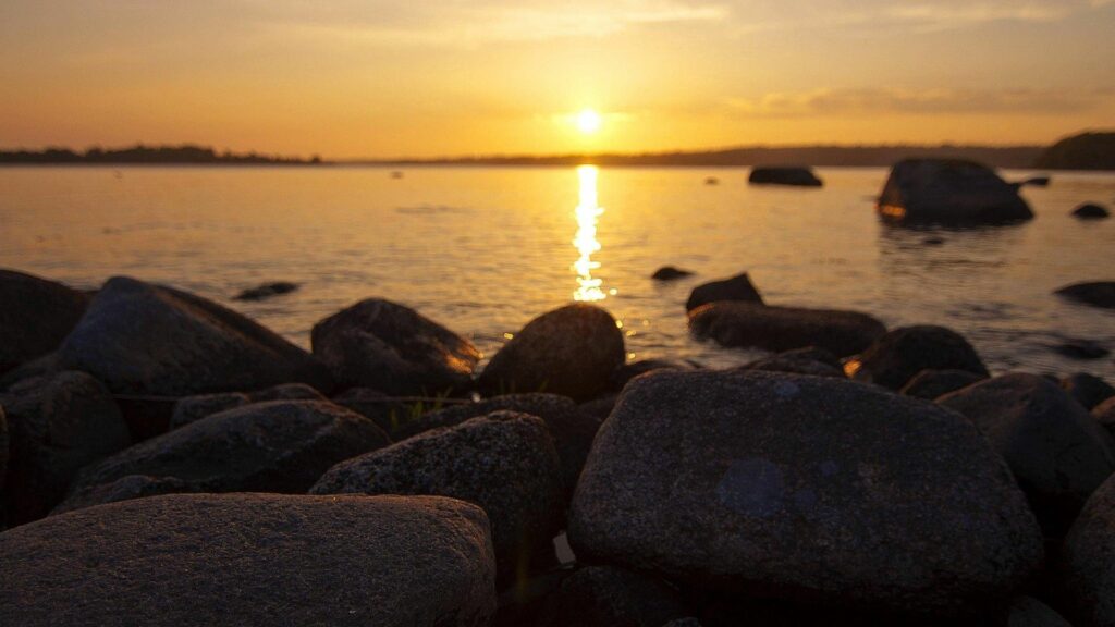 Smooth rocks on tranquil beach at sunset with golden sunlight and soft orange sky wallpaper background