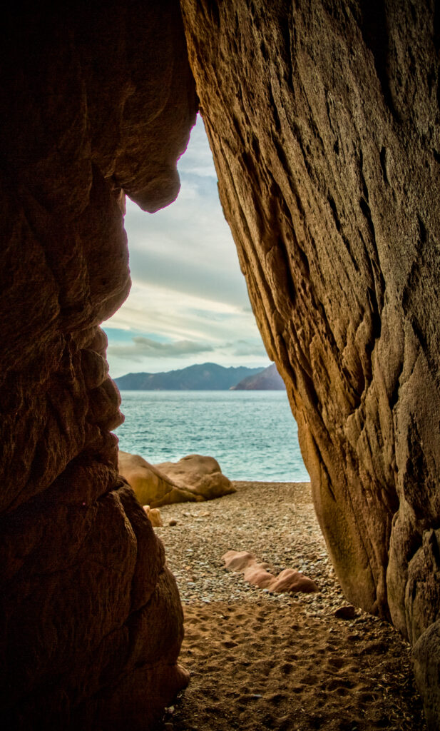 View from cave entrance to pebble beach peaceful sea and mountains under cloudy sky wallpaper