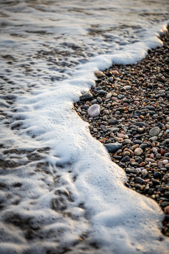 Gentle wave with soft foam rolling over smooth colorful pebbles beach wallpaper background