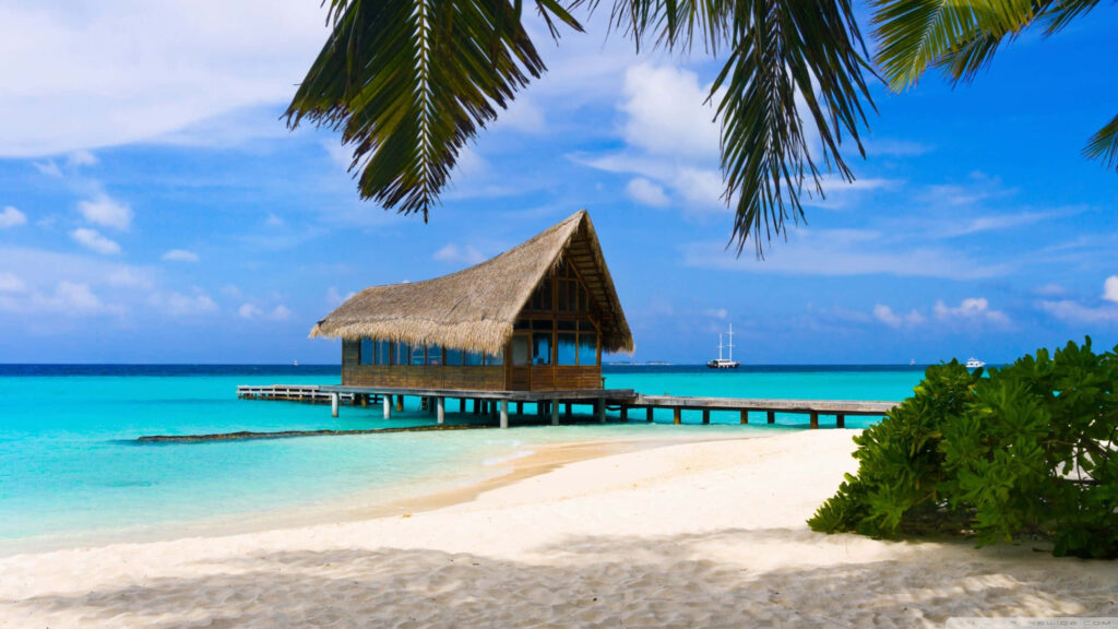 Tranquil Beach Scene: Thatched Bungalow Over Turquoise Waters Wallpaper