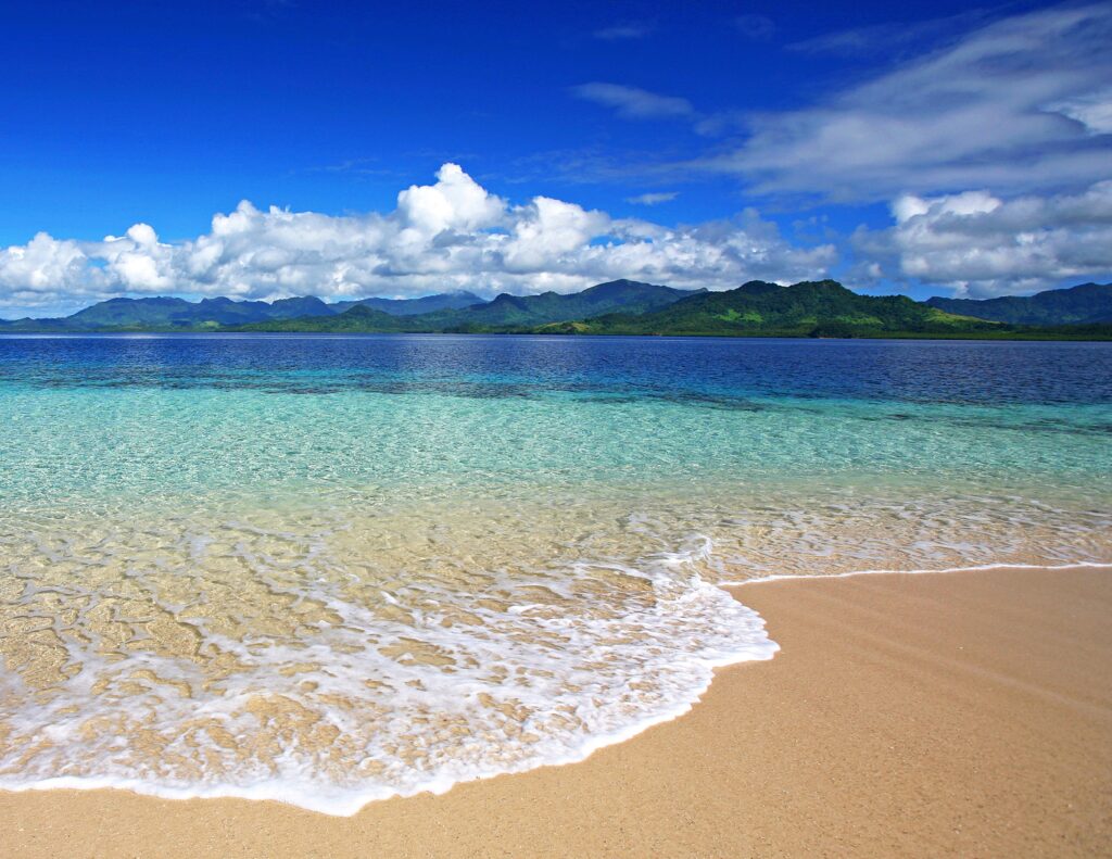 Tranquil beach with turquoise water soft sand green mountains and blue sky wallpaper background