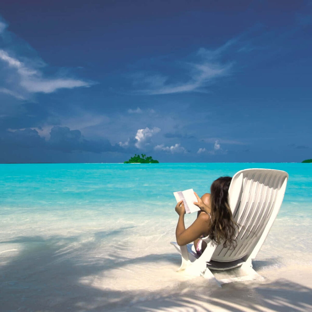 Tranquil Beach Scene: Woman Reading by Crystal-Clear Waters Wallpaper