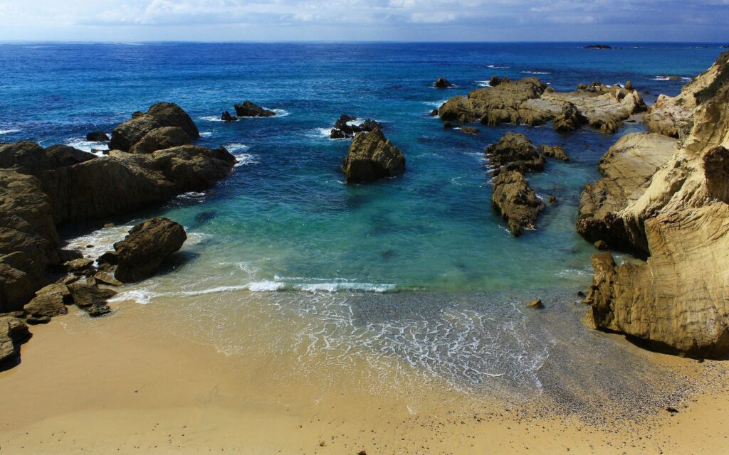 Tranquil beach wallpaper with gentle waves golden sand rugged rocks and clear blue sea sky