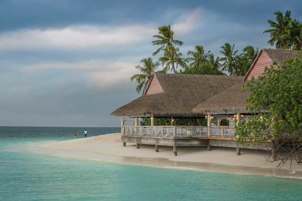 Tranquil Beachfront Wallpaper: Charming Thatched-Roof Haven