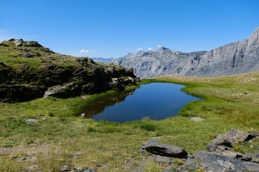 Clear blue lake in lush green valley with rugged mountains under bright sky nature wallpaper