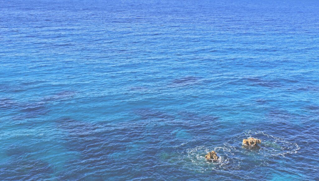 Tranquil blue ocean wallpaper with gentle waves and two small rocks in serene seascape view
