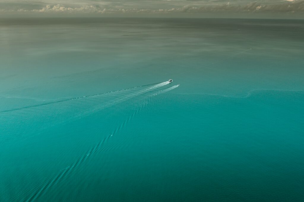 Aerial view of calm blue sea with single boat gliding creating gentle ripples serene wallpaper