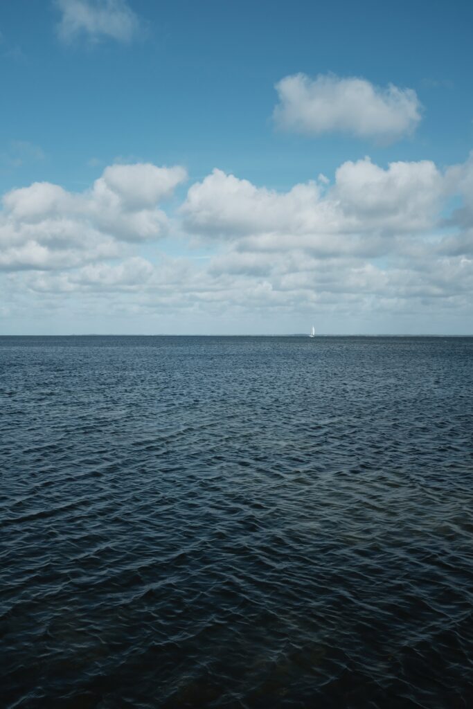 Tranquil wallpaper of blue sea with gentle ripples bright sky fluffy clouds and distant boat