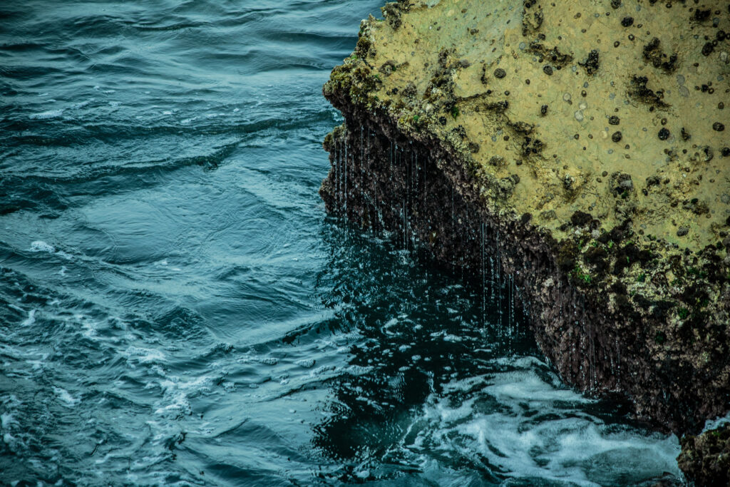 Clear blue sea water laps rugged stone edge with green moss and delicate water drops wallpaper background