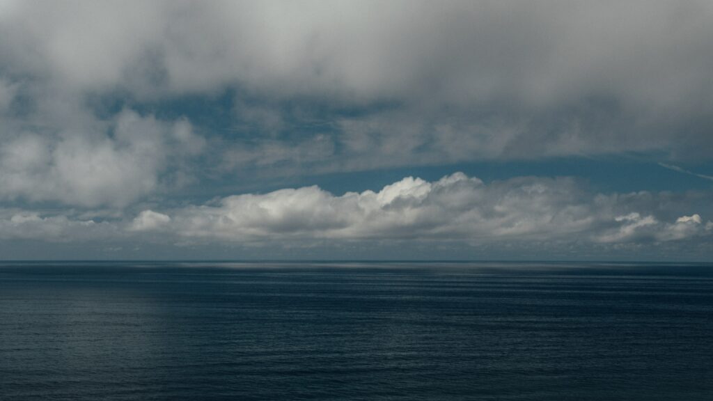 Calm blue seascape with distant horizon and soft billowing clouds serene wallpaper background