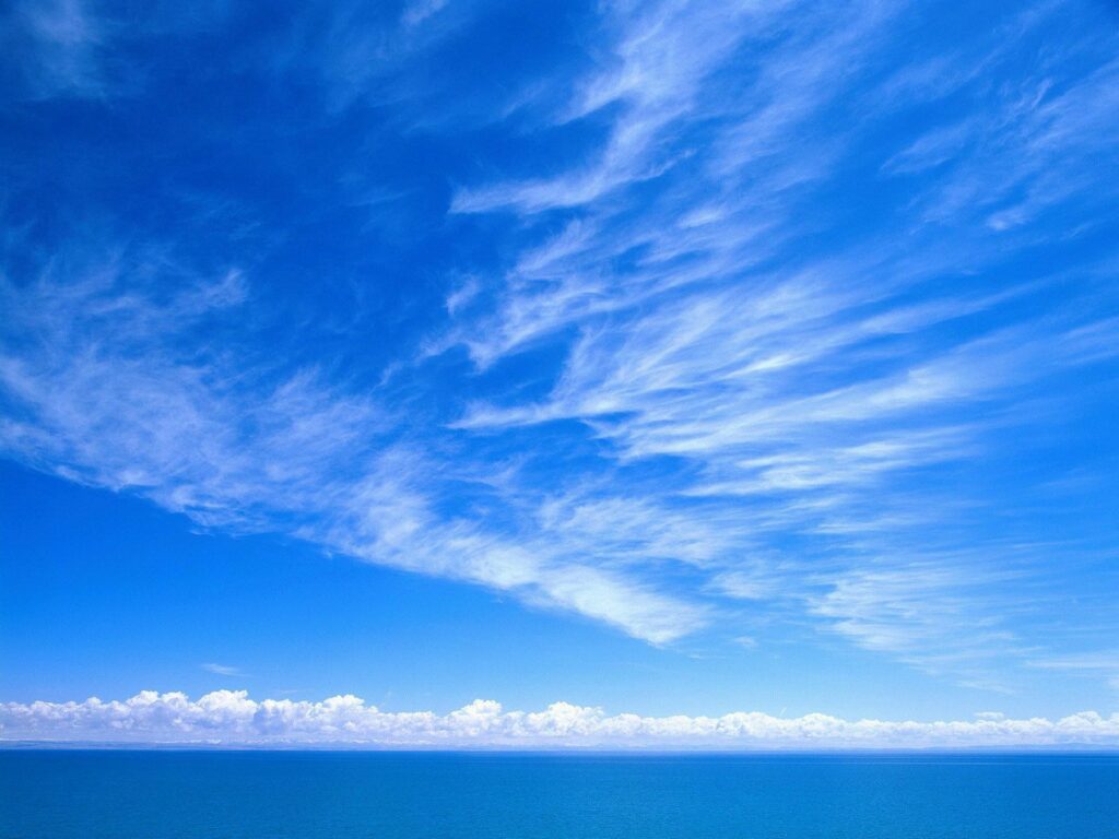 Tranquil blue sky with wispy white clouds over calm horizon peaceful wallpaper background