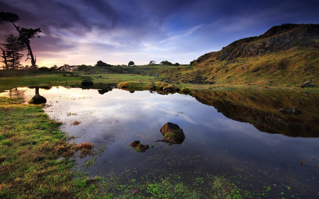 Tranquil bog reflecting rugged mountains and dramatic evening sky with lush green grass wallpaper
