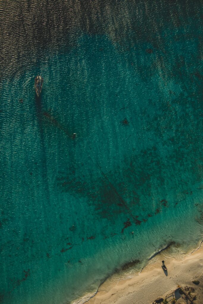 Aerial view of turquoise coastline with anchored ship and sunlit sandy shore wallpaper background