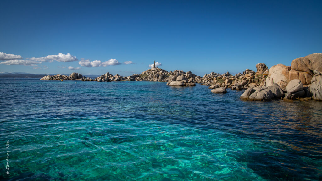 Tranquil coastal bay with turquoise waters rocky cliffs and lighthouse under clear blue sky wallpaper