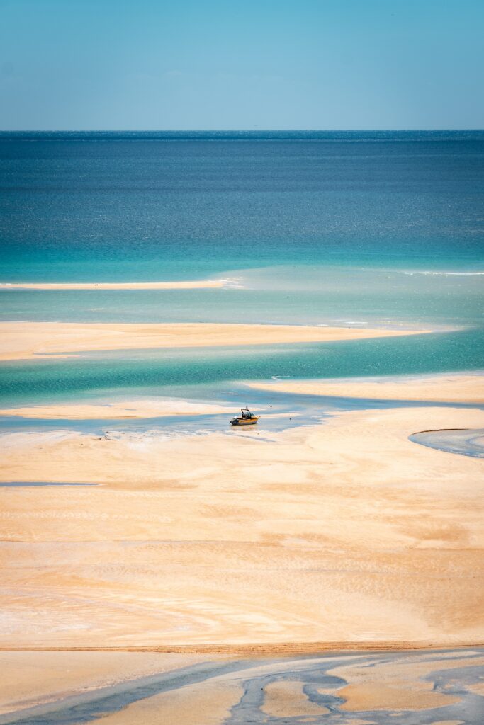 Small boat on sandy beach with turquoise waters and clear sky peaceful coastal scenery wallpaper