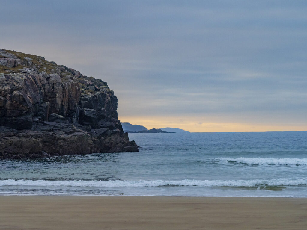 Tranquil coastal wallpaper with soft sand rugged rocks gentle waves and glowing cloudy horizon