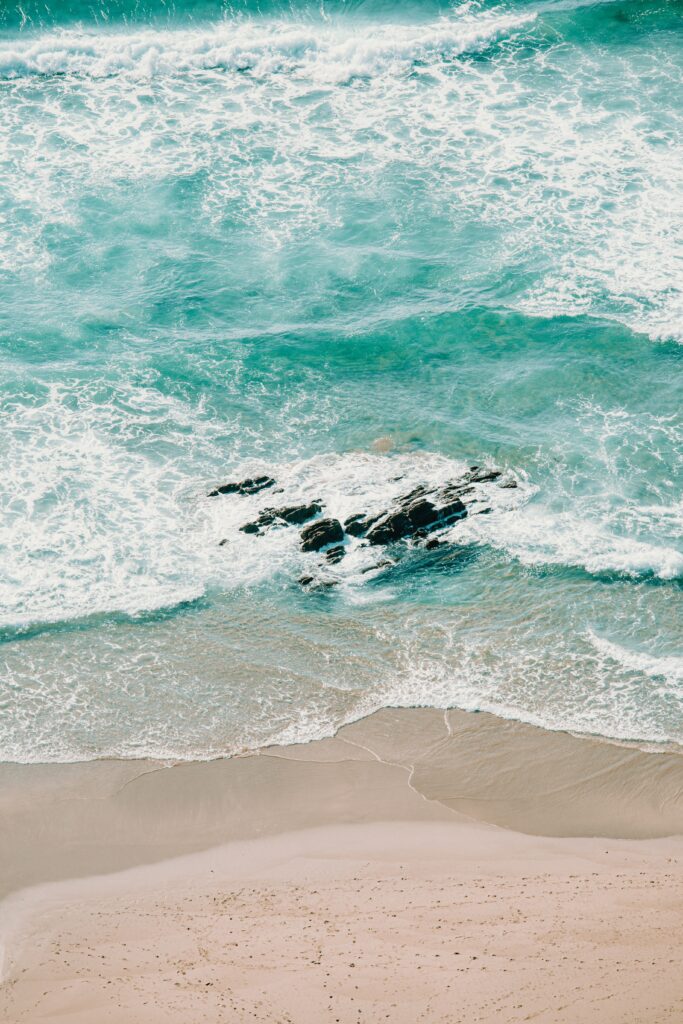 Tranquil coastal wallpaper with golden sand turquoise sea foamy waves and exposed rocks