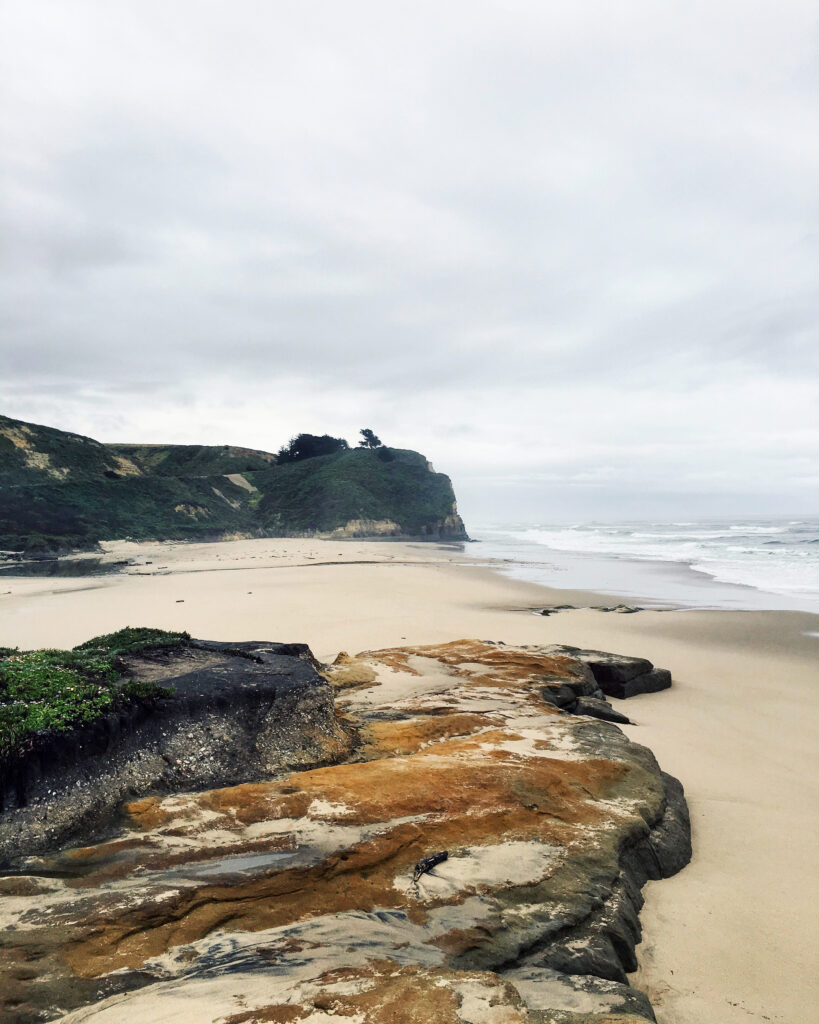 Serene coastal beach with sandy shore rugged rocks gentle waves and cloudy sky landscape wallpaper