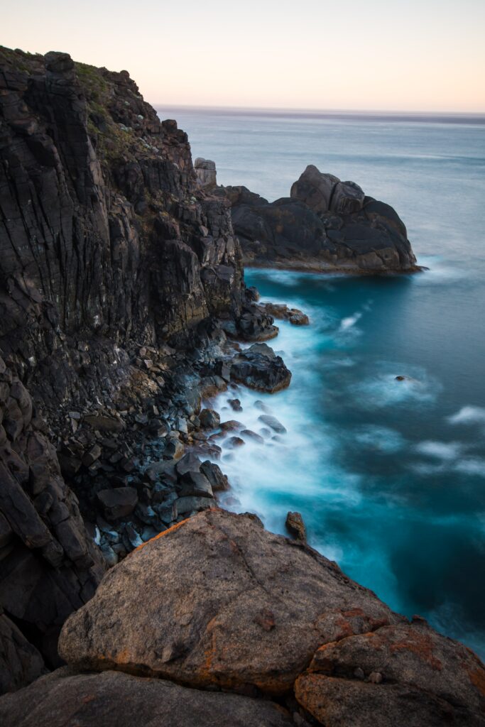 Breathtaking coastal cliffs and boulders with gentle blue ocean waves under a serene sky wallpaper