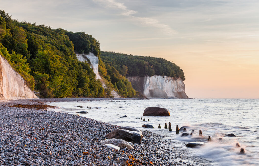Tranquil coastal scene with white cliffs pebble beach lush green trees and soft pastel sky wallpaper