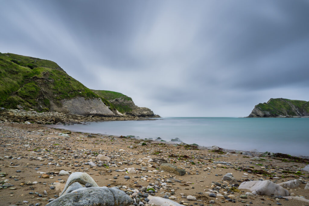 Tranquil coastal landscape wallpaper with rugged rocks pebbled beach and lush green cliffs