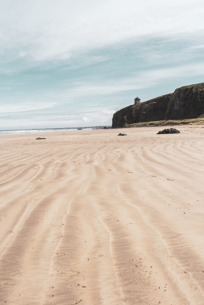 Tranquil coastal landscape with sandy patterns cliffs distant mountains pale blue sky wallpaper
