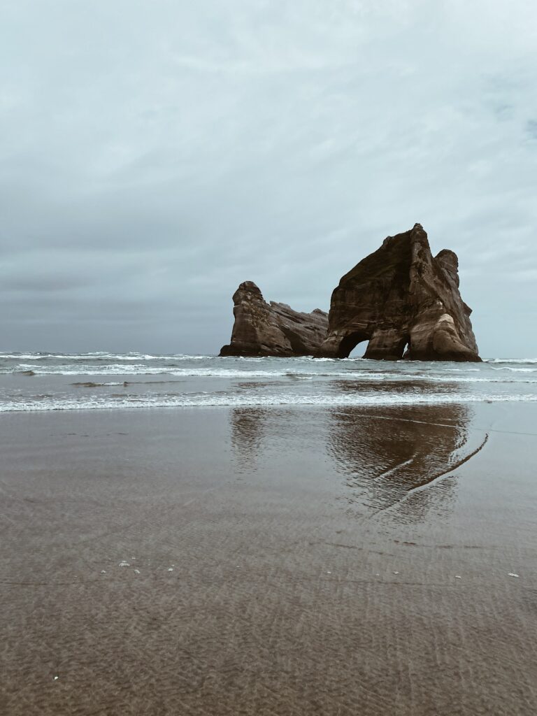 Dramatic coastal rock formation reflected on wet sand under cloudy sky tranquil beach wallpaper