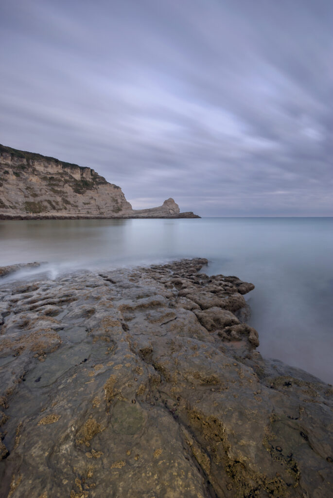 Serene coastal wallpaper with rugged rocks smooth sea pastel sky dramatic cliffs background