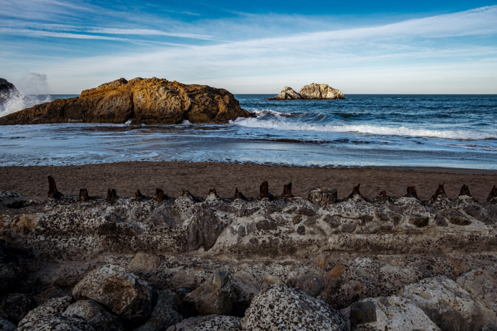 Coastal wallpaper with rugged rocks smooth stones rolling sea waves under vibrant blue sky