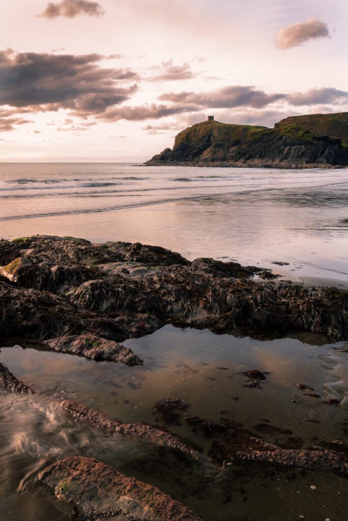 Tranquil coastal shoreline with rugged rocks tidal pools gentle waves and sunset cliff building Wallpaper