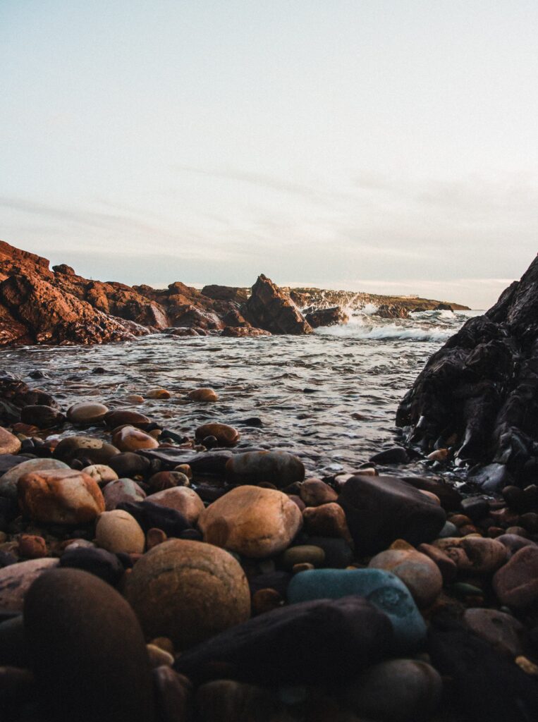 Tranquil coastal scene with smooth stones jagged rocks gentle waves and soft pastel sky wallpaper