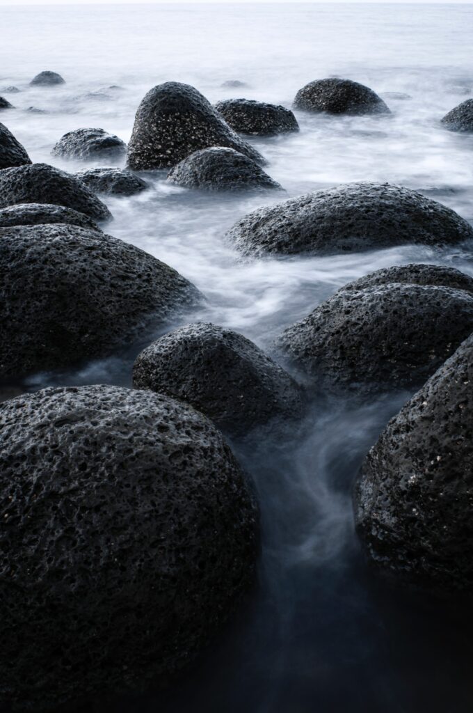 Smooth rounded stone blocks in misty coastal water with soft blue gray tones serene scene Wallpaper