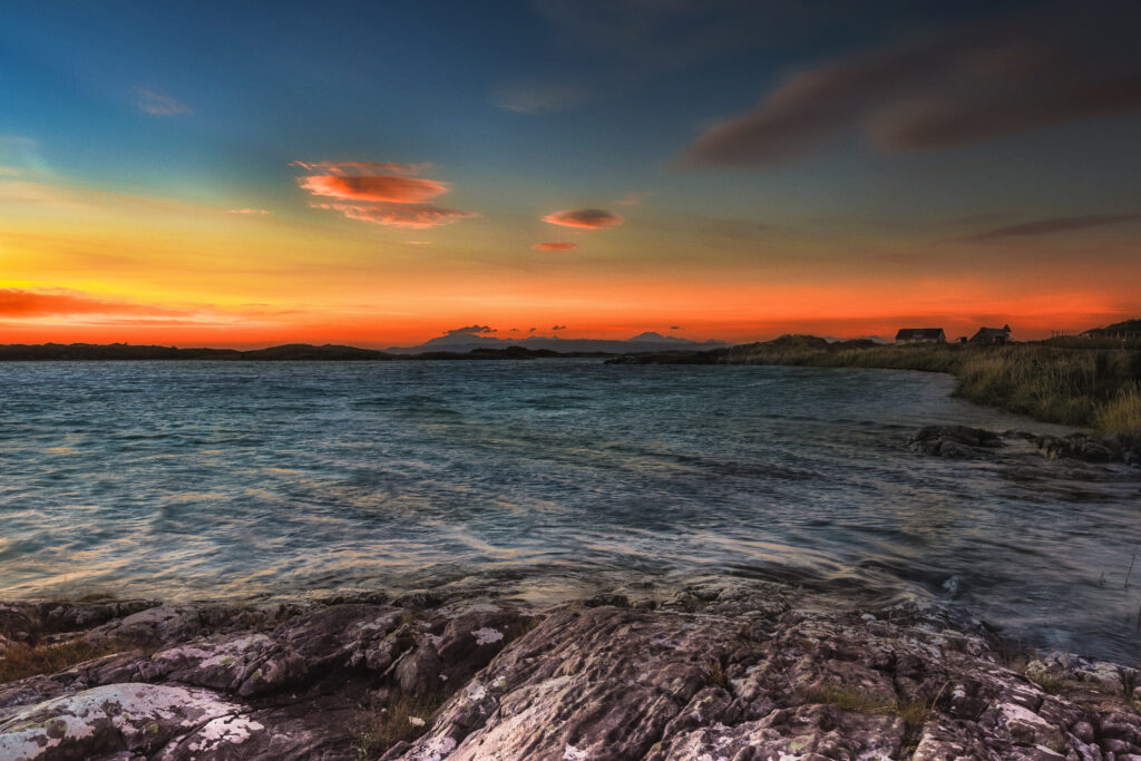 Tranquil coastal sunset with rugged cliffs gentle waves and distant shore buildings wallpaper background