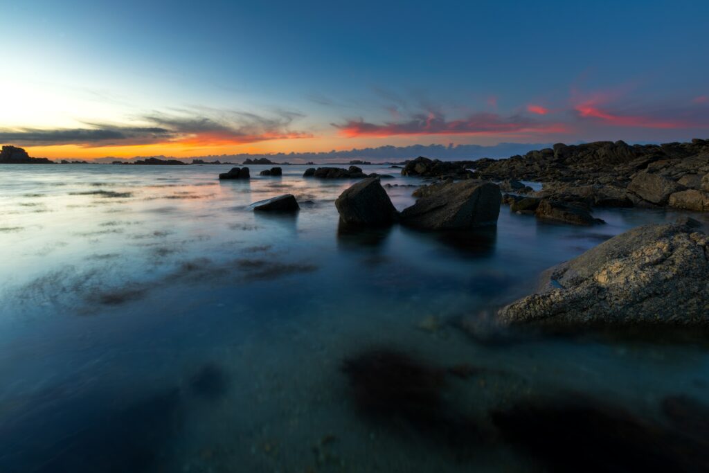 Sunset coastal landscape with rugged rocks calm waters reflecting blue and orange hues wallpaper
