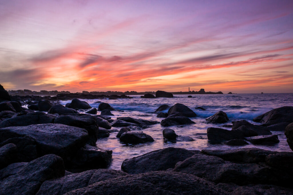 Sunset coastal landscape with rugged stones shoreline gentle waves vibrant purple pink sky wallpaper