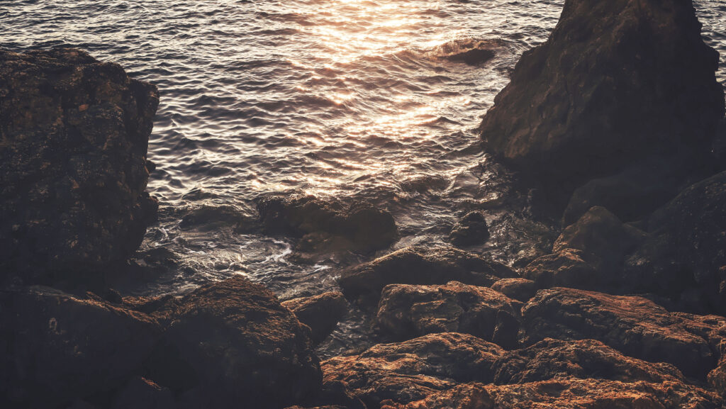 Sunset coastal wallpaper with golden light reflecting on gentle waves and rocky shore