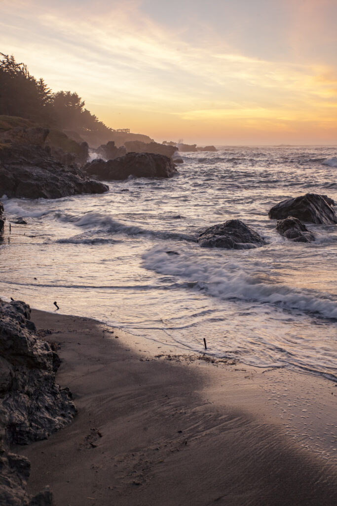 Serene coastal wallpaper with rugged rocks sandy beach gentle waves and warm sunset hues