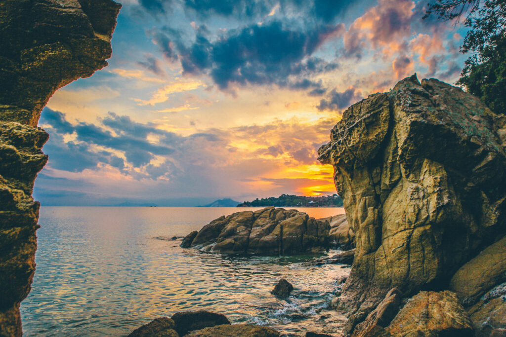 Serene coastal sunset with rugged rocks smooth stones and tranquil sea nature wallpaper background