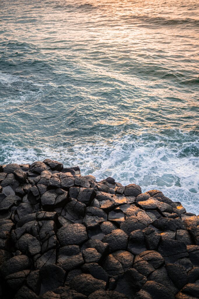Rugged coastal rocks with gentle waves at sunset wallpaper natural textures blue gold hues